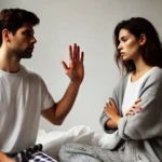 Casal em discussão na cama. Homem com mão estendida, mulher de braços cruzados.