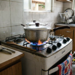 Cozinha brasileira tradicional com chama no fogão, botijão de gás aparente e utensílios domésticos cotidianos.